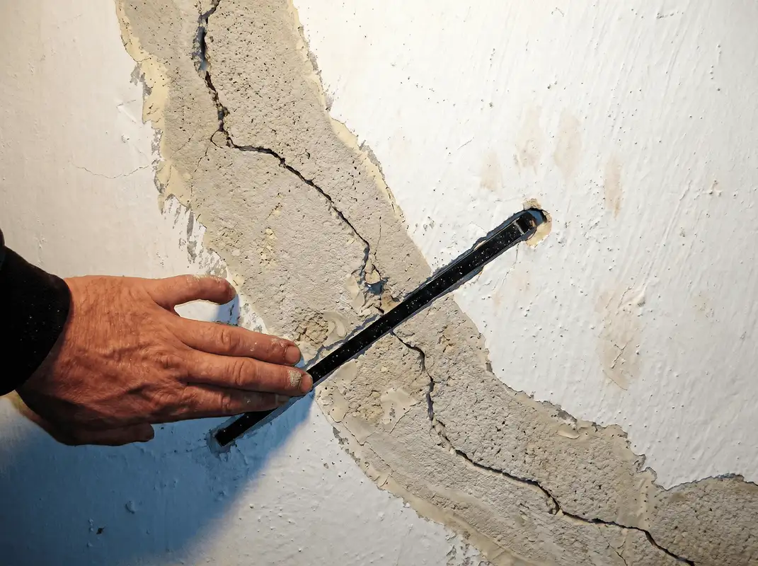 A wall with a large crack is being inspected by a professional in Bakersfield, CA