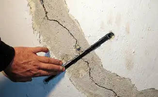 A wall with a large crack is being inspected by a professional in Bakersfield, CA